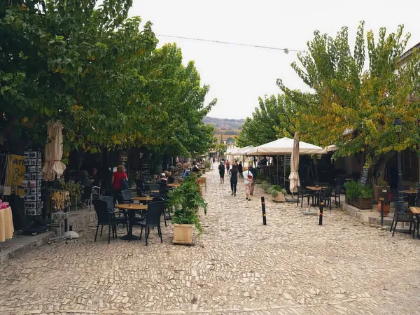 Tree-lined cobbled square with café tables in Omodos